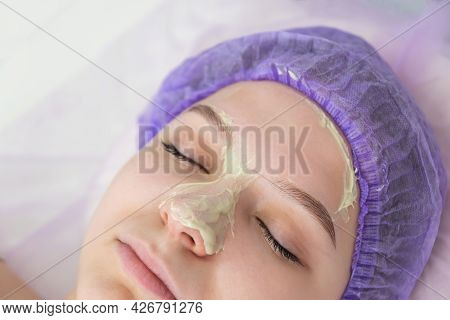 In The Beauty Salon, The Beautician Puts A Mask Of Green Clay On The Face Of A Young Girl. Daily Fac
