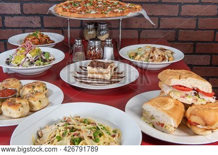 Pizzaria Feast Of A Full Table Of Food Consisting Of Pizza, Pasta, Sandwiches, Dessert, And Salad To