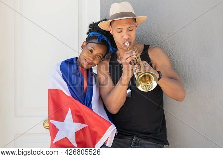 Smiling Latina Woman Leaning On Latino Man Playing The Trumpet