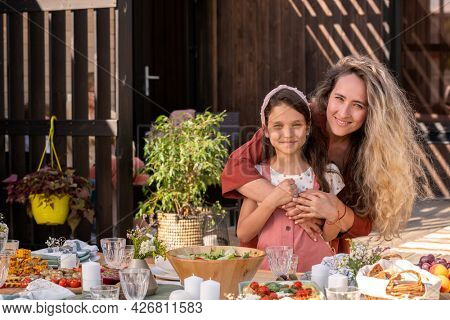Portrait of smiling beautiful woman hugging her little daughter from behind when they are standing at dinner table