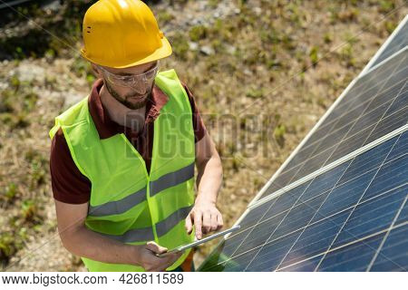 Solar panel mounter in vest, goggles and hardhat checking information on tablet computer