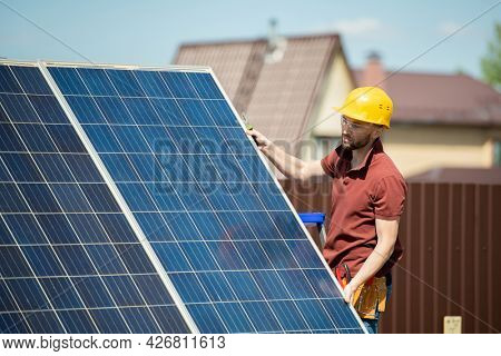 Mounter in hardhat and protective goggles installing solar panel in backyard of house