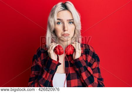 Young blonde girl listening to music using headphones depressed and worry for distress, crying angry and afraid. sad expression. 
