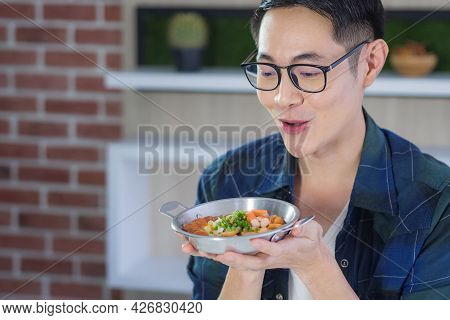 Asian Young Man Wearing Glasses Sitting Looking At The Fried Egg Served On Pan With Colorful Topping