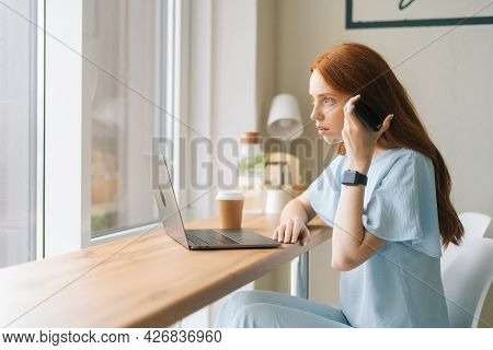 Side View Of Serious Young Female Sudent Listening Audio Message On Smartphone Sitting At Table With