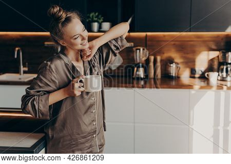 Young Pretty Relaxed Woman In Comfy Pajama Stretching From Sleep Early In Morning While Holding Cup 