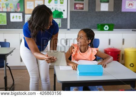 African american female teacher with digital tablet teaching a girl at elementary school. school and education concept