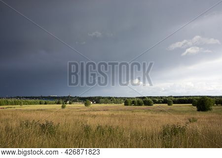 Landscape With Dramatic Sky And Unripe Wheat Field At Rainy Summer Season. Dirt Road With Dark Storm