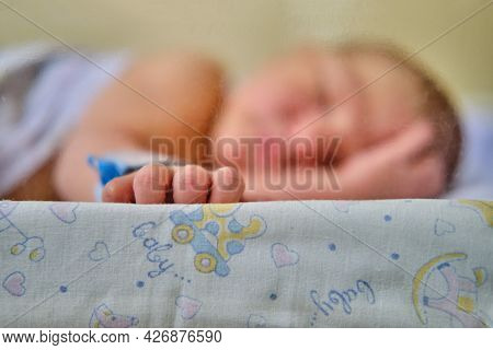 Hand Newborn Baby With A Maternity Hospital Bracelet On His Arm Is Sleeping In A Crib. A Newly Born 