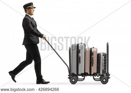 Full length profile shot of a bellboy walking and pushing a trolley cart with suitcases isolated on white background