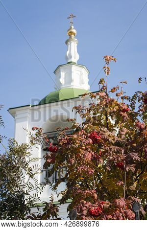 Against The Background Of A Blue Sky, A White Bell Tower With A Green Roof Rises. Bells Are Visible 