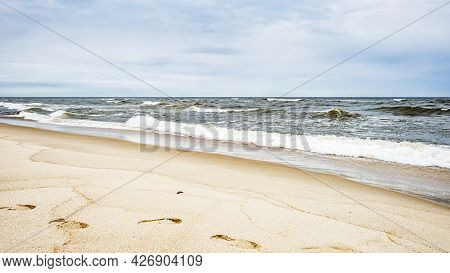 Sea Waves And Footprints On The Sand On The Beach And Overcast Sky