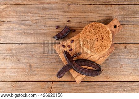 Dry Carob Pods And Carob Powder Over Wooden Background