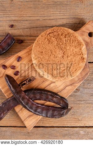 Dry Carob Pods And Carob Powder Over Wooden Background