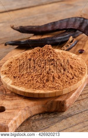 Dry Carob Pods And Carob Powder Over Wooden Background