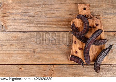 Dry Raw Carob Pods On Wooden Background