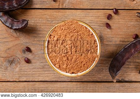 Dry Carob Pods And Carob Powder Over Wooden Background, Top View