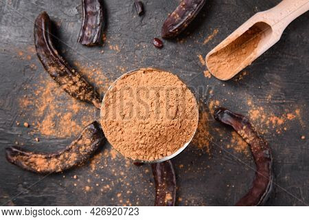 Dry Carob Pods And Carob Powder Over Dark Background. Organic Healthy Ingredient For Vegan Vegetaria