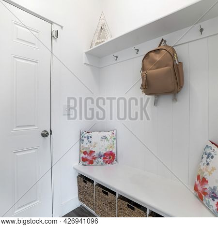 Square Frame Interior Of A White Mud Room With White Door, Built-in White Bench And Wall Mounted Hoo