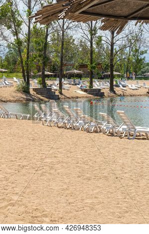 A Lot Of Free White Plastic Sun Beds On The Sand Near The Lake. Sun Loungers On The Beach
