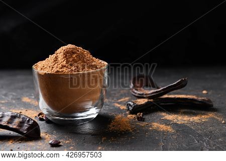 Dry Carob Pods And Carob Powder On A Dark Background. Organic Healthy Ingredient For Vegan Vegetaria