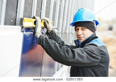 Plasterer builder worker with level examining metal profile facade plate installation