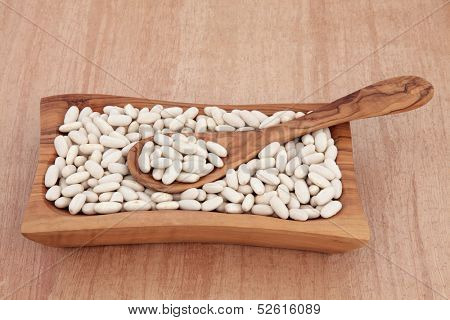 Cannellini bean dried food ingredient in an olive wood bowl over papyrus background.