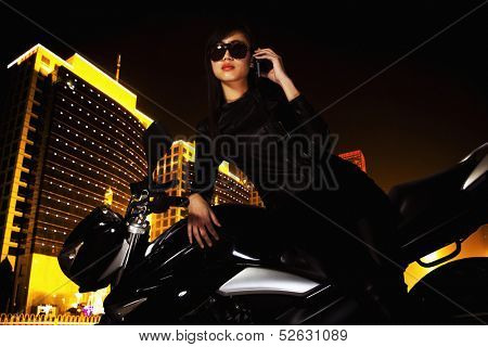 Beautiful young woman with sunglasses talking on the phone and leaning on her motorcycle