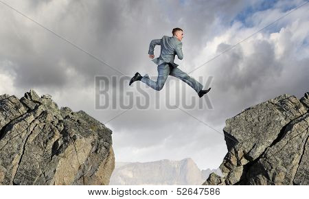 Young businessman jumping over mountain gap. Risking in business