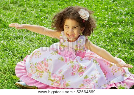 Little  girl sits with outstretched hands to sides on grassy lawn spreading hem of her dress