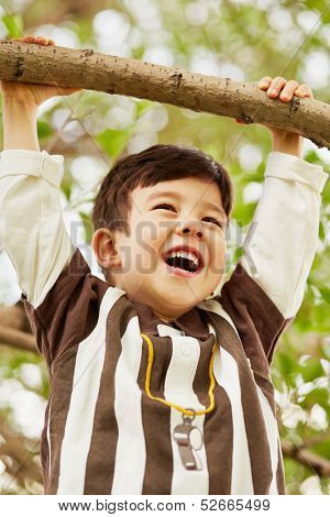 Closeup portrait of laughing little boy who hang on branch grasping at it with hands