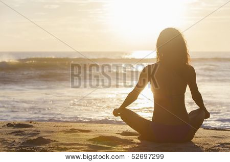 A relaxed sexy young brunette woman or girl wearing a bikini sitting on a deserted tropical beach at sunset or sunrise