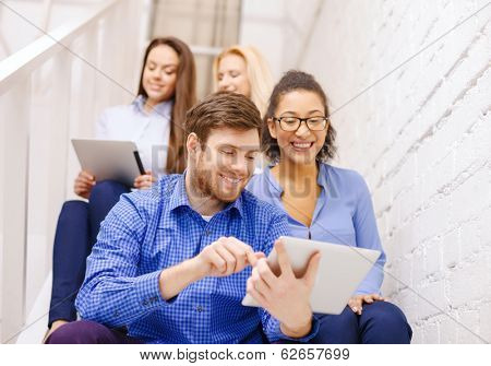 business, technology and startup concept - smiling creative team with tablet pc computer sitting on staircase