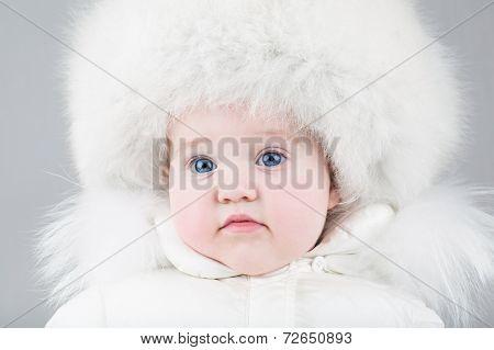 Funny Little Baby Girl Wearing A Huge Fur Hat And A White Winter Snow Suit
