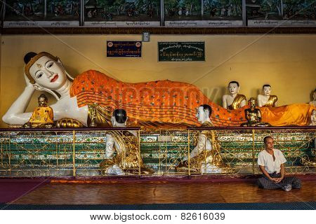 YANGON, MYANMAR - JANUARY 3, 2014: Man meditating near statue of Recumbent Buddha in Shwedagon Paya pagoda