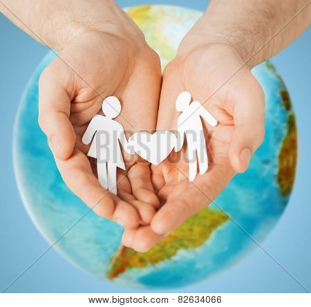 people, population, charity and love concept - close up of human hands holding paper couple with heart shape over earth globe and blue background