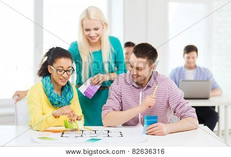 education, interior design and office concept - smiling interior designers with color samples and blueprint in office