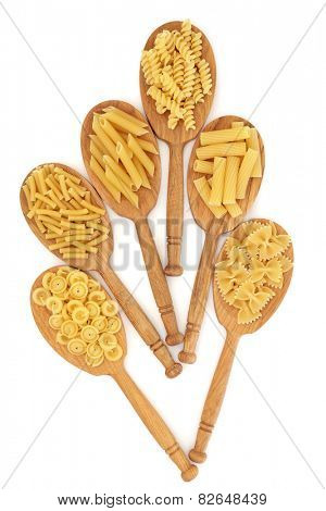Dried pasta food selection in oak wood spoons over white background.