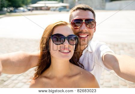 love, wedding, summer, dating and people concept - smiling couple wearing sunglasses making selfie in city