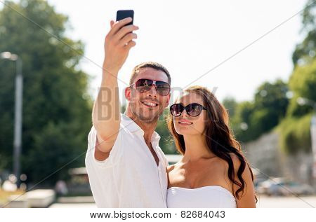 love, wedding, summer, dating and people concept - smiling couple wearing sunglasses making selfie with smartphone in park