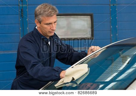 Portrait Of A Mature Mechanic Cleaning Windshield With A Cloth At Garage
