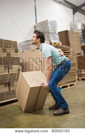 Side view of worker with backache while lifting box in the warehouse
