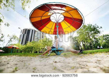 Boy And Girl Sitting Under A Big Colorful Beach Umbrella. Boy And Girl Holding Hands