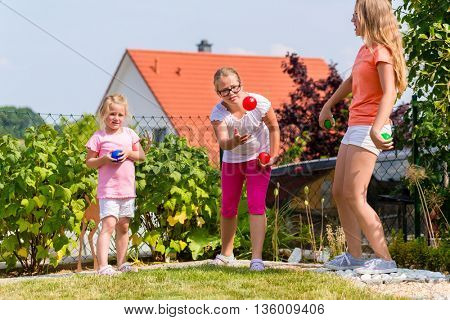 Three sisters playing bocce in garden front or their home in summer