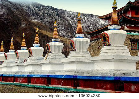 Ganzi, China - April 19 2012: A row of white dagobas with yellow ringed spires at the Xiabosang Tibetan monastery   
