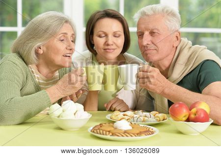 Cute family portrait , adult daughter with senior parents drinkig tea
