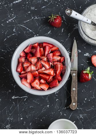 Chopped strawberries and the jar with whole grain flour on a dark stone background. Ingredients for making strawberry pie