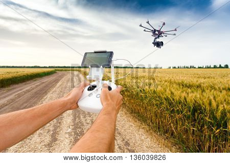 Demonstration of unmanned copter. Man controls quadrocopter flight. Flying the copter over a field of wheat. Remote control in a man's hands.