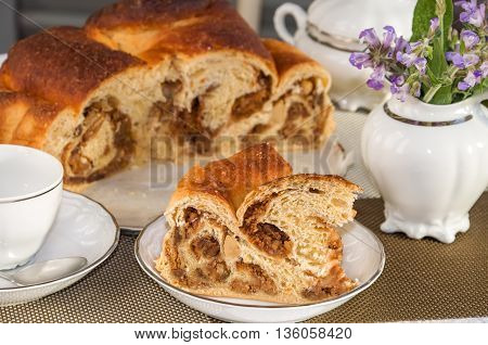 Good piece of typical italian flavorous home baked cake La Gubana with sophisticated stuffing (hazelnuts fruit chocolate walnut raisins honey etc.) with purple flowers of salvia on the table covered for tea. Traditionally bake for Christmas and Easter.