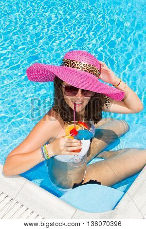 woman in a hat enjoying cocktail in a swimming pool
